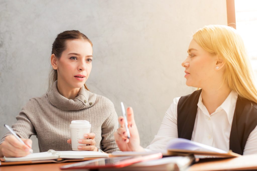 Duas mulheres sentadas lado a lado com papéis sobre a mesa recebendo feedback 360