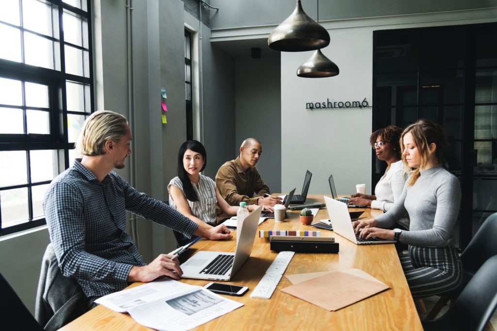 Pessoas em volta de uma mesa com notebooks e papéis discutindo sobre missão, visão e valores.