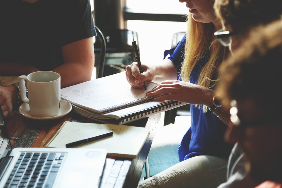 Pessoas em volta de uma mesa com cadernos, canetas e notebooks aprendendo como fazer brainstorming