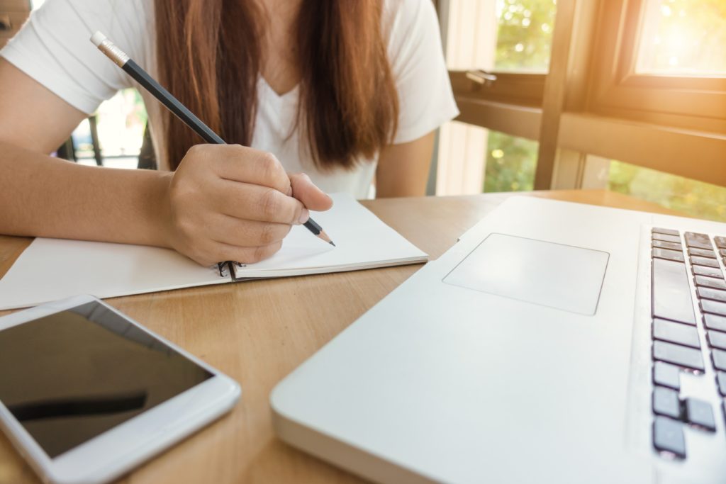 Mulher estudando sobre o financeiro de uma empresa sentada em uma mesa com notebook e caderno