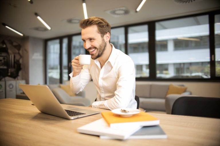 Empresário feliz sentado em uma mesa com notebook, livros e café, demonstrando sua satisfação no trabalho