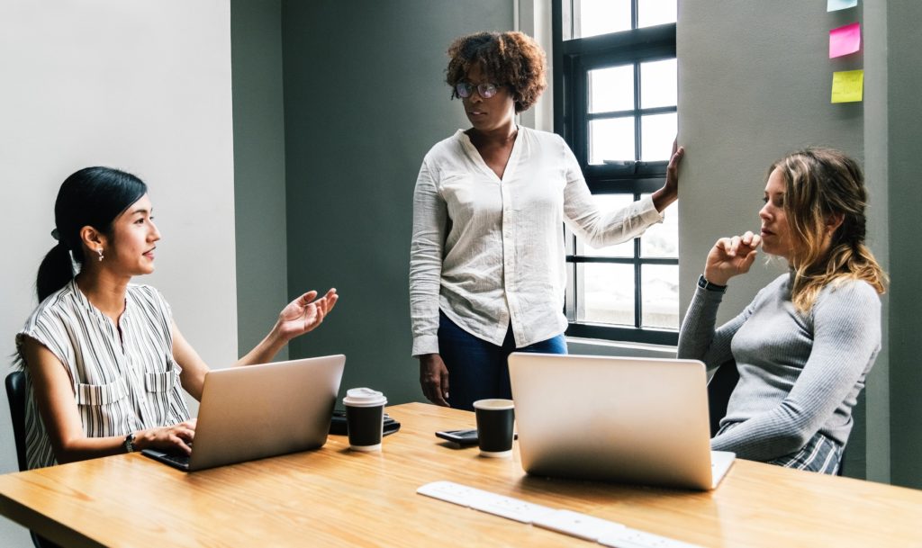 Três mulheres de diferentes etnias em uma reunião profissional.