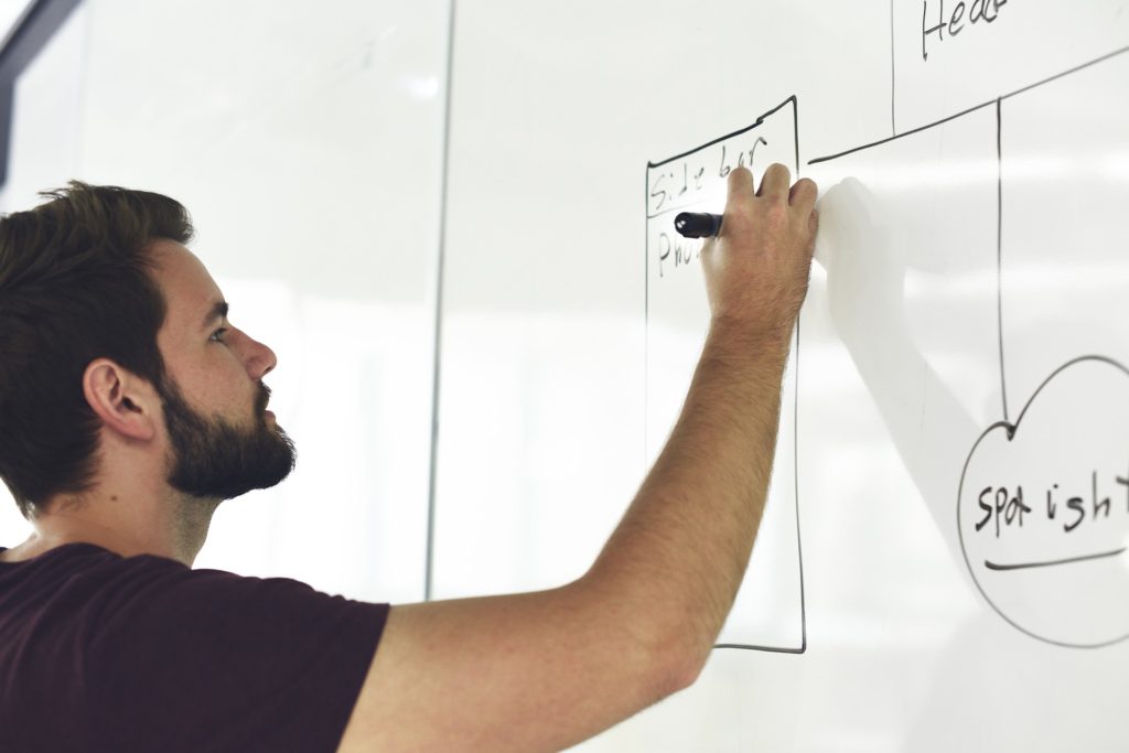 Um homem escrevendo no quadro branco com um canetão, expondo ideias para aumentar a criatividade no trabalho