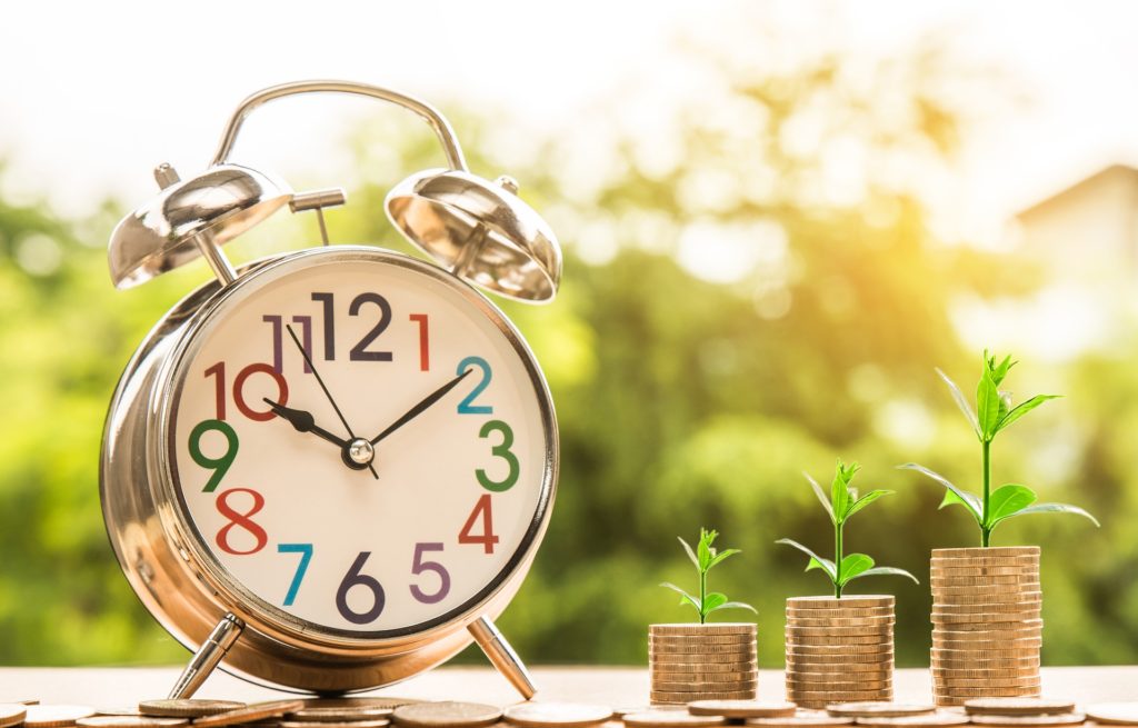Imagem de um relógio ao lado de moedas que dão origem a pequenas plantas simbolizando como a gestão de tempo e dinheiro são o principal desafio profissional para quem procura progredir no mercado