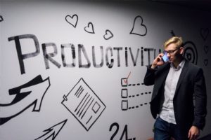 Homem falando ao celular sobre negócios e oportunidades em frente a uma parede na qual está escrito "productivity"